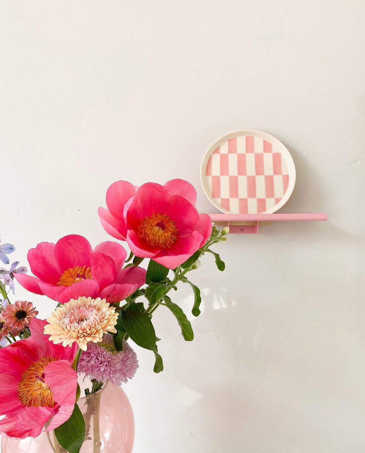 Wandplankje in roze Studio Mippe met een bordje van Loods 5 met daarnaast in vaas mooie bloemen